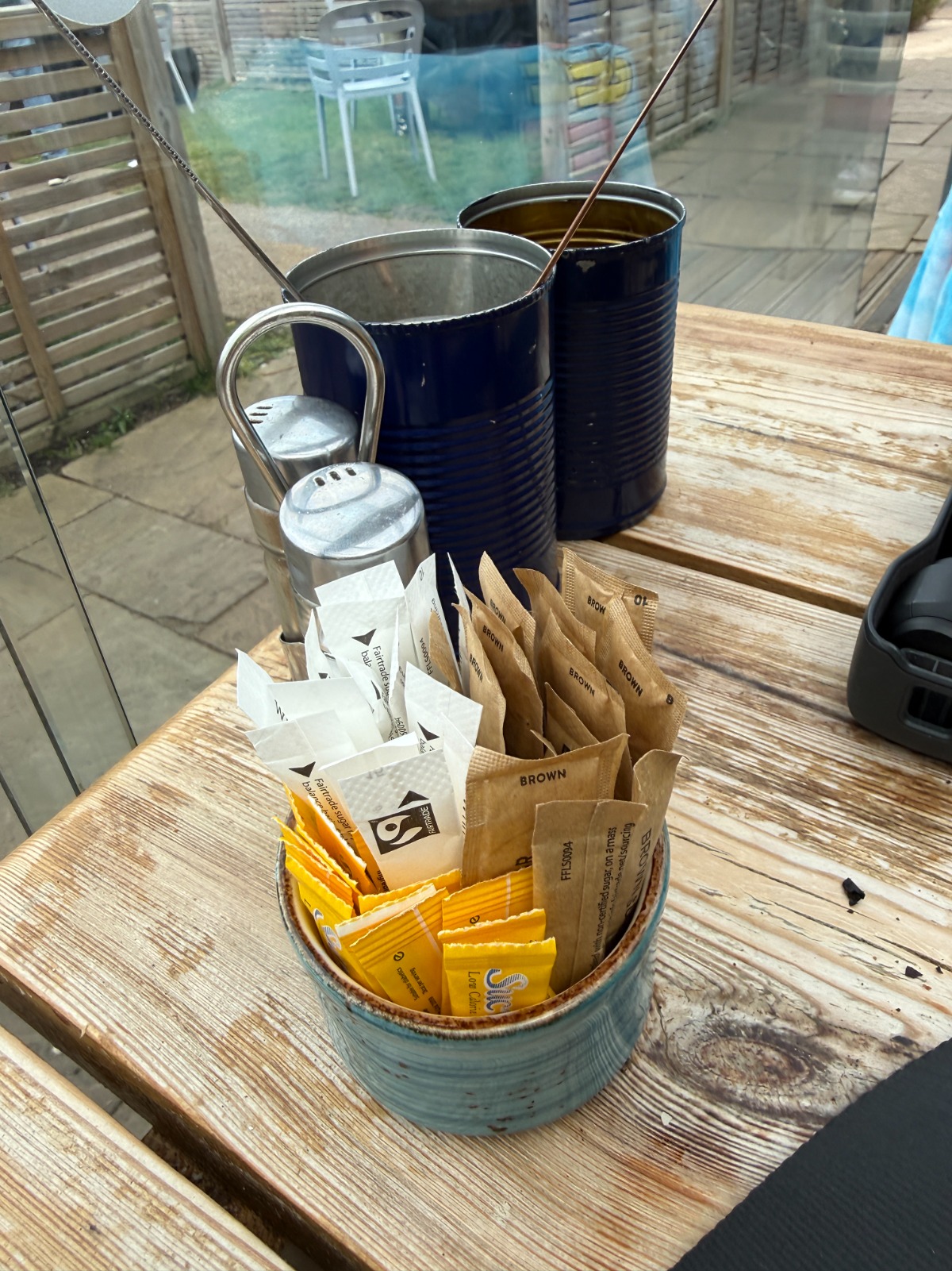Sugar and condiments caddy on a table at The Aerodrome Café, Elstree EGTR, with Fairtrade white and brown sugar sachets, sweeteners and metal salt and pepper shakers.
