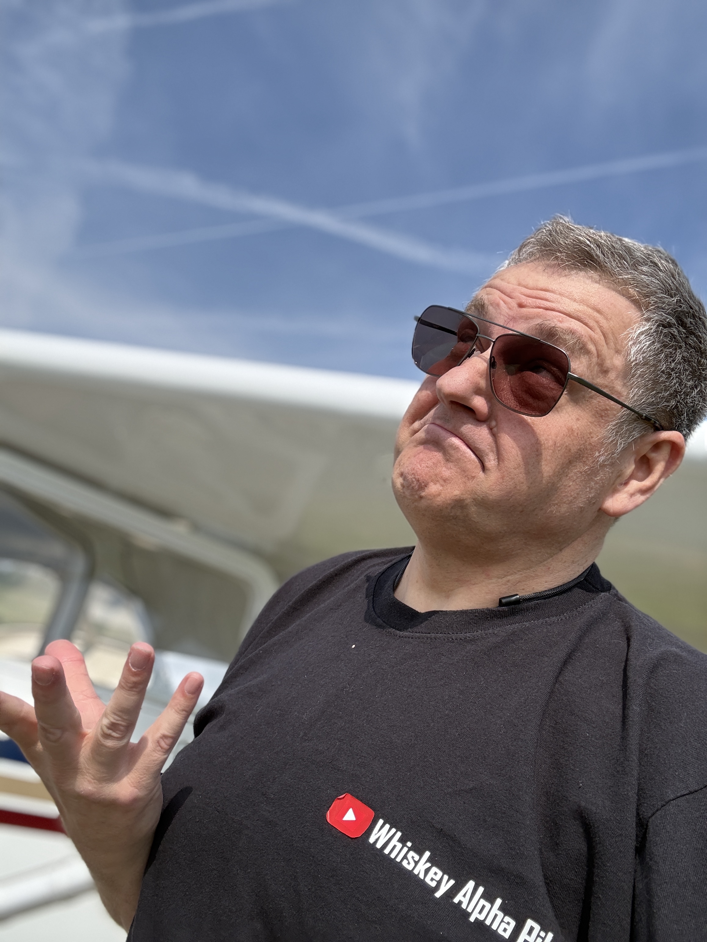 Wayne Allen, WhiskeyAlphaPilot, in sunglasses and a Whiskey Alpha Pilot T-shirt, shrugging next to KK's wing at Elstree after a rusty solo flight